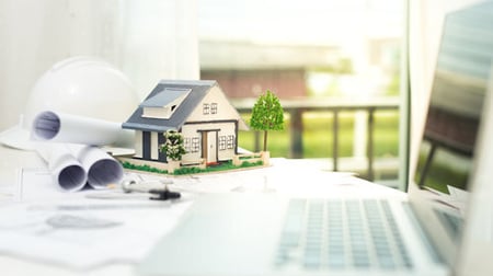 Model of a house on a desk near architecture papers and a computer